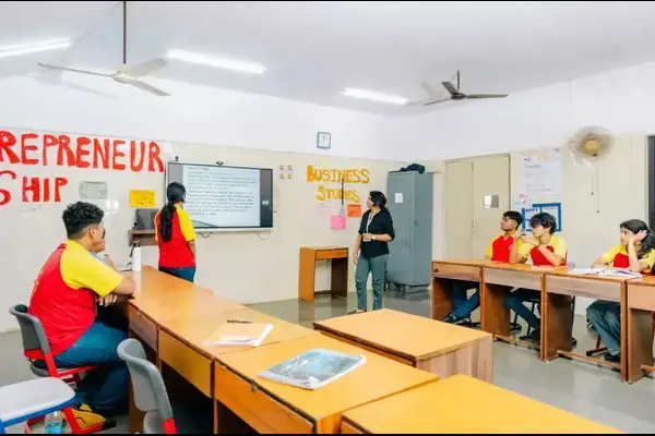Students in a classroom face a screen with a teacher
