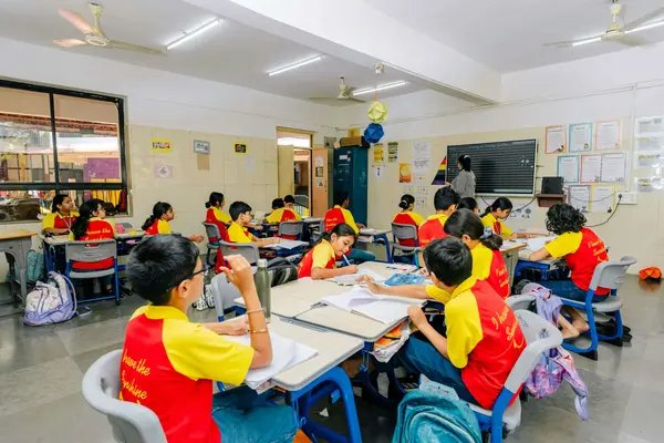 A classroom with students sitting at tables while a teacher writes on the chalkboard