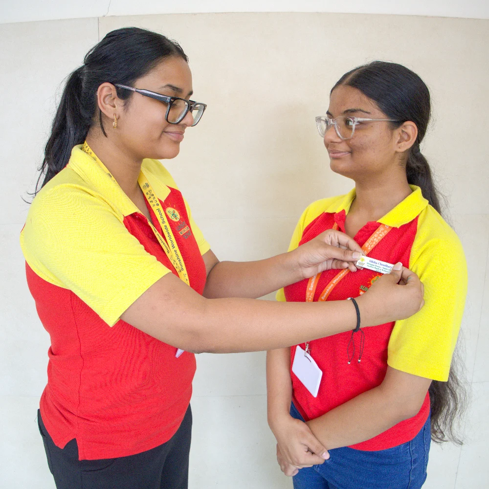 Two female students stand facing each other, with one pinning a badge on the other’s uniform